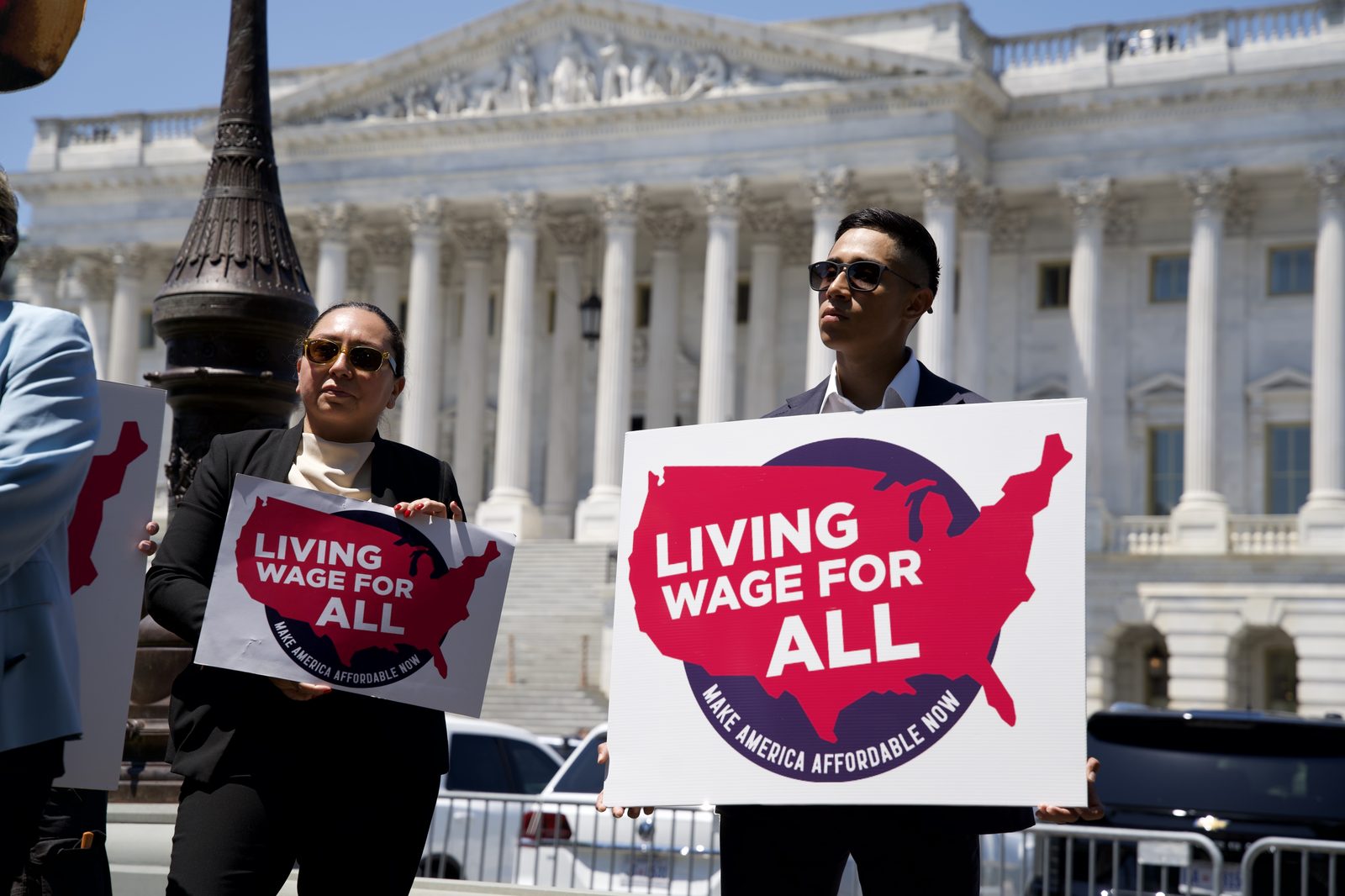 A coalition member holds a Living Wage For All sign in front of the U.S. Capitol at the Senate launch, June 25, 2026